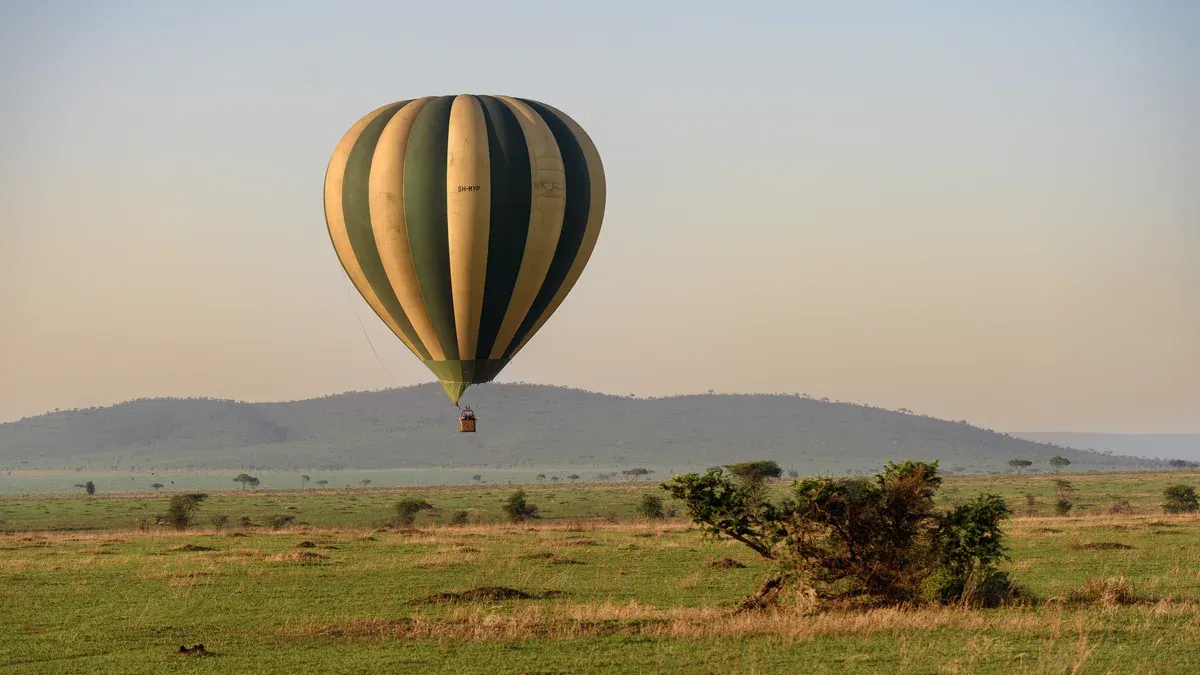 A striped hot air balloon floating over the Serengeti plains at sunrise on a Serengeti safari package